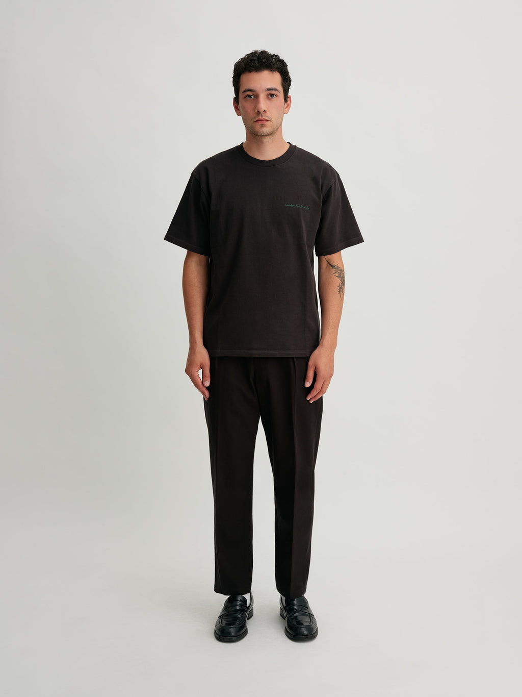 Saturdays NYC. 1Tuck Tapered Pants. Full-body view of model wearing the black chinos, showcasing the tapered fit and single tuck at the waist.