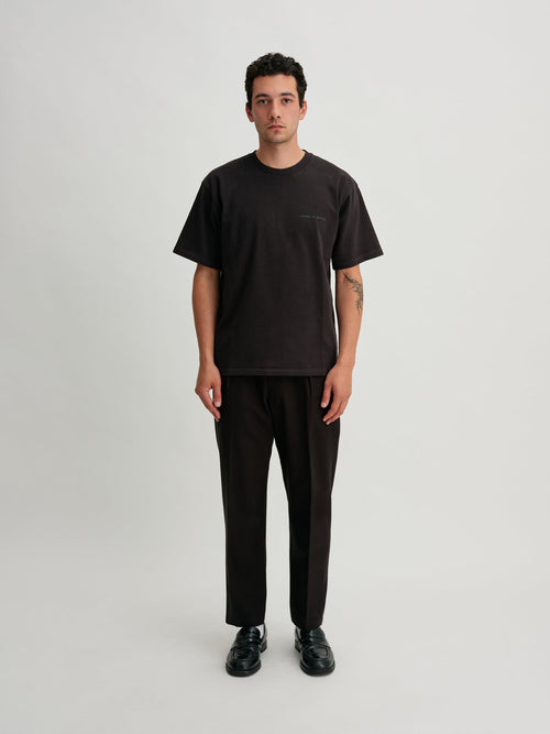 Saturdays NYC. 1Tuck Tapered Pants. Full-body view of model wearing the black chinos, showcasing the tapered fit and single tuck at the waist.