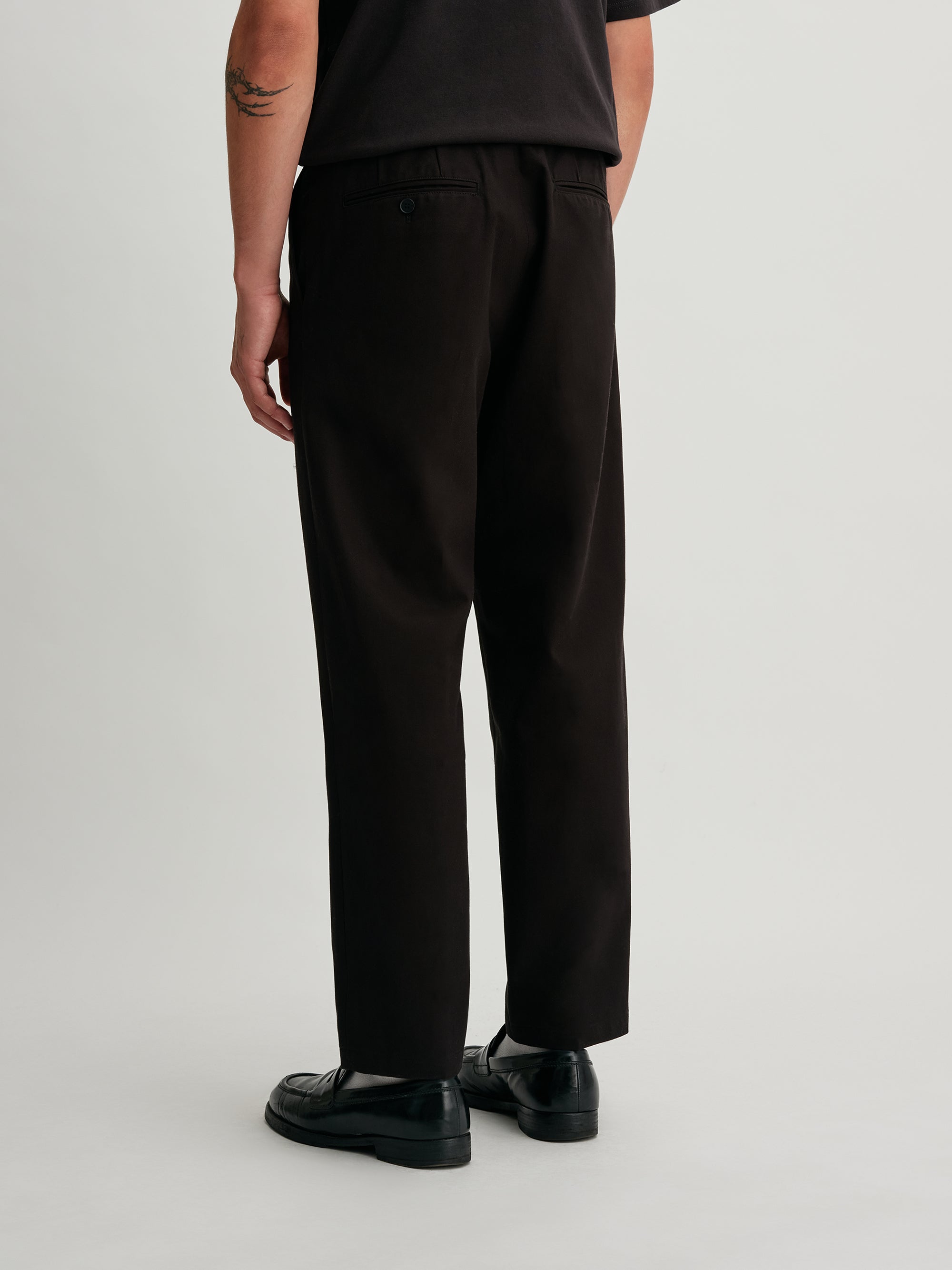 Saturdays NYC. 1Tuck Tapered Pants. Back view of model wearing the black chinos, showcasing the tailored fit, relaxed silhouette, and clean back design.